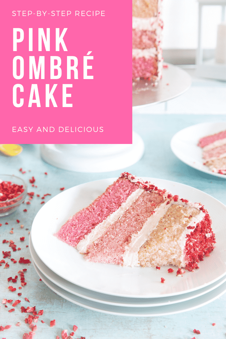 A slice of pink ombre cake on a stack of small white plates. The cake has three layers, each an increasingly intense shade of pink. The sponges are layered with pale pink frosting and the outside is decorated with freeze dried strawberry pieces. A small piece has been cut from the slice. Caption reads: Step-by-step recipe pink ombre cake. Easy and delicious.