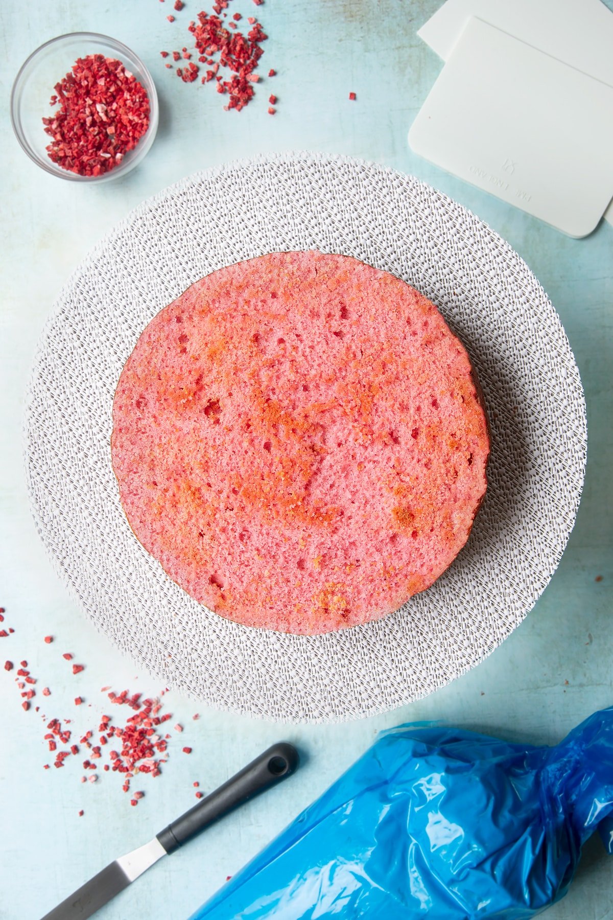 The first layer of a pink ombre cake (the brightest pink shade) on a cake turntable. 