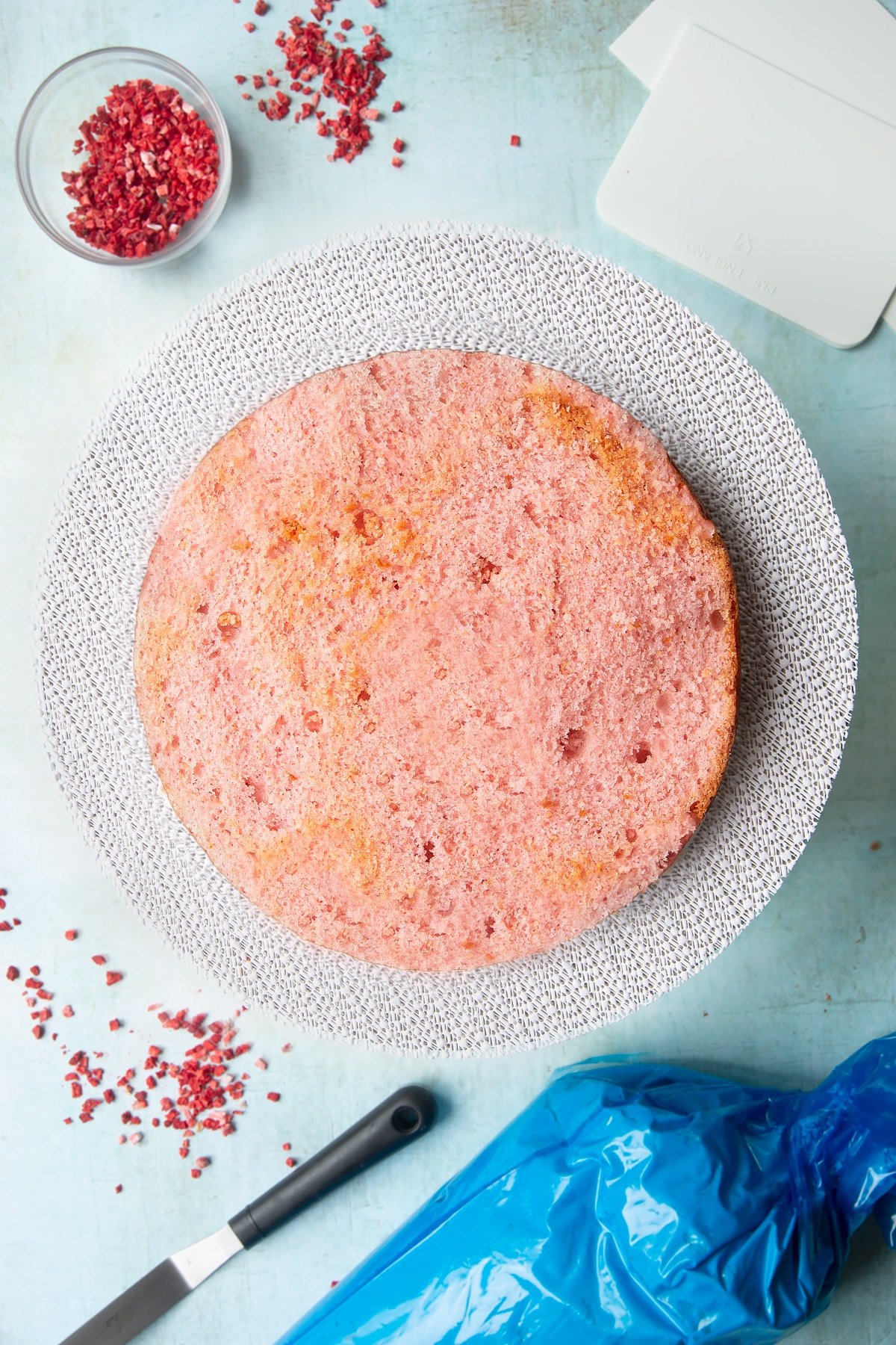 The first two layer of a pink ombre cake (the brightest and mid pink shade) on a cake turntable, with pale pink frosting sandwiched between them.
