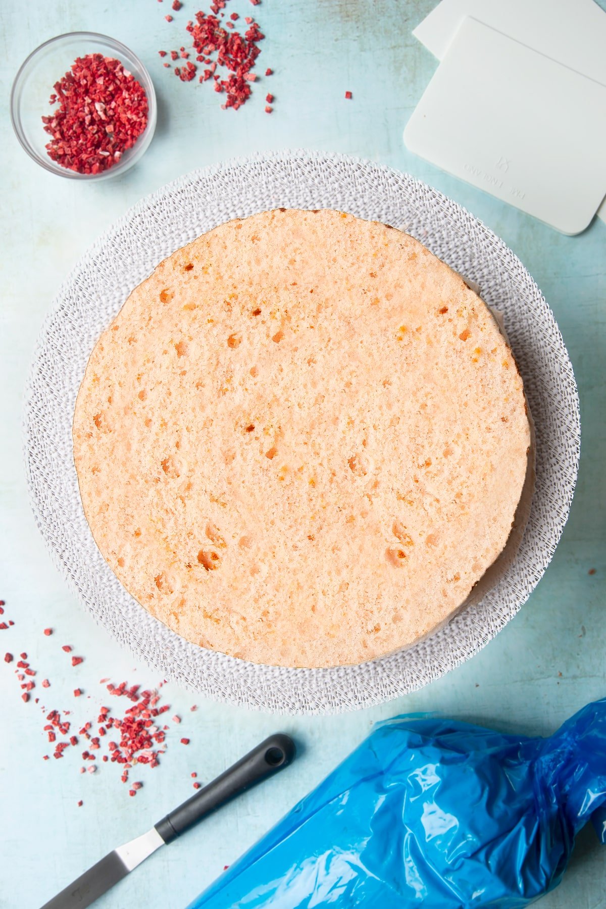 The three layers of a pink ombre cake from brightest to palest pink, stacked on a cake turntable, with pale pink frosting sandwiched between them.