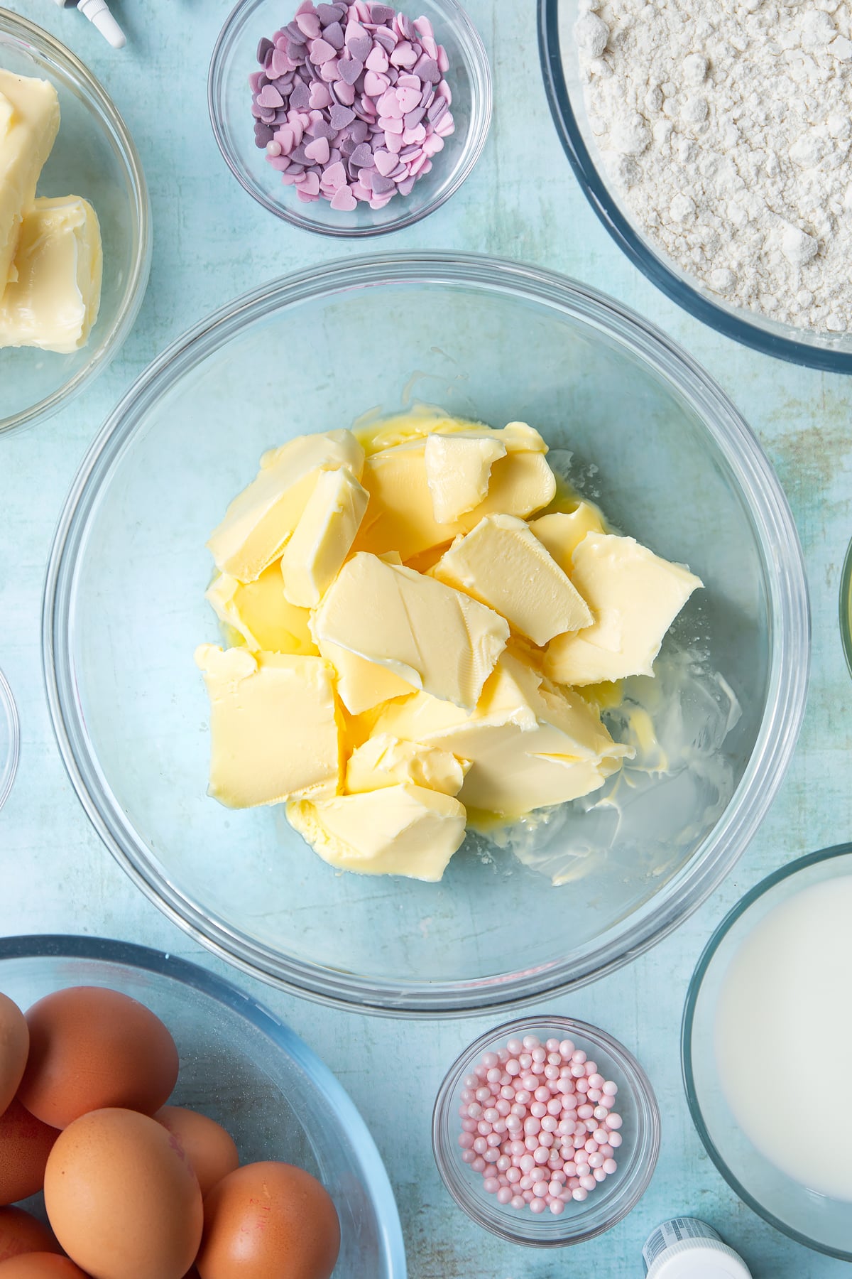 Softened butter in a mixing bowl. Ingredients to make pink ombre cake surround the bowl.