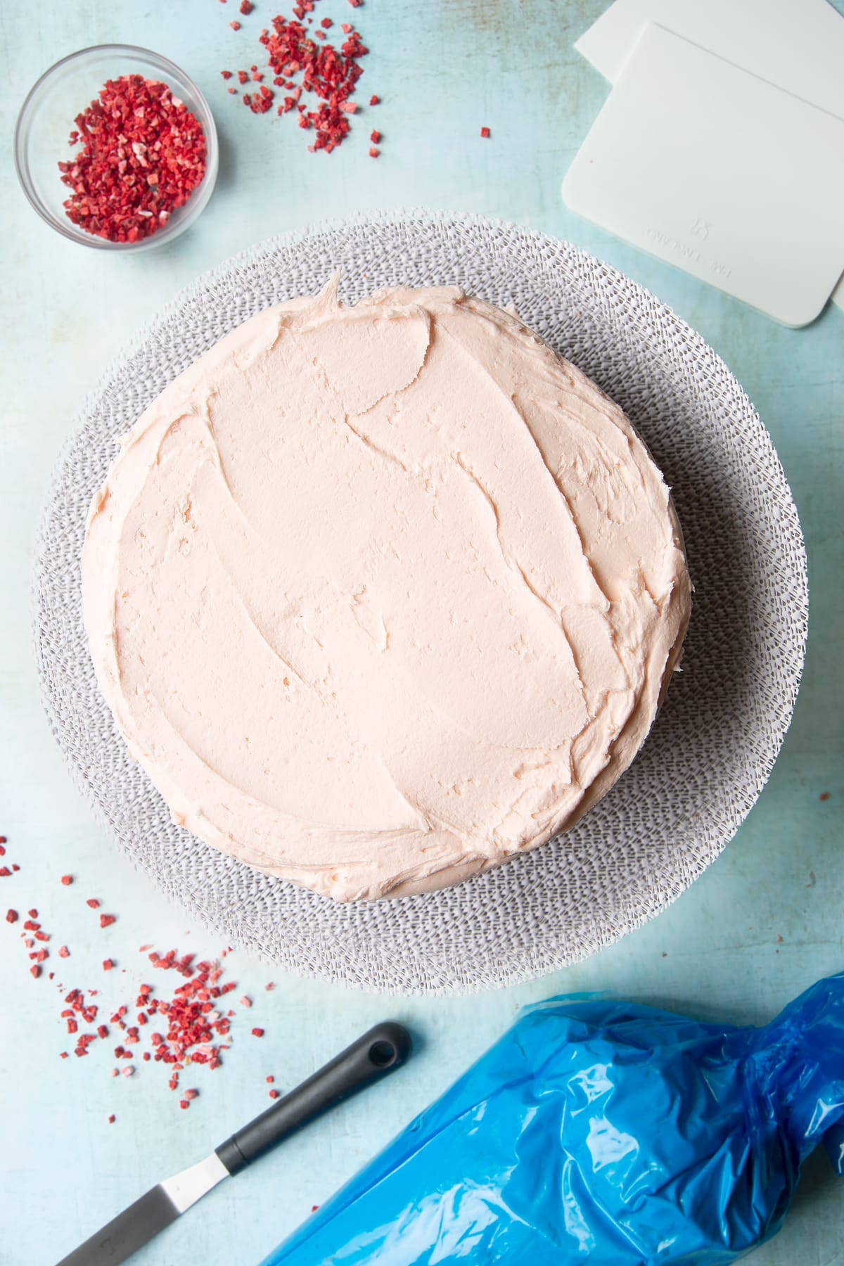 The first two layer of a pink ombre cake (the brightest and mid pink shade) on a cake turntable, with pale pink frosting sandwiched between and on top of them.