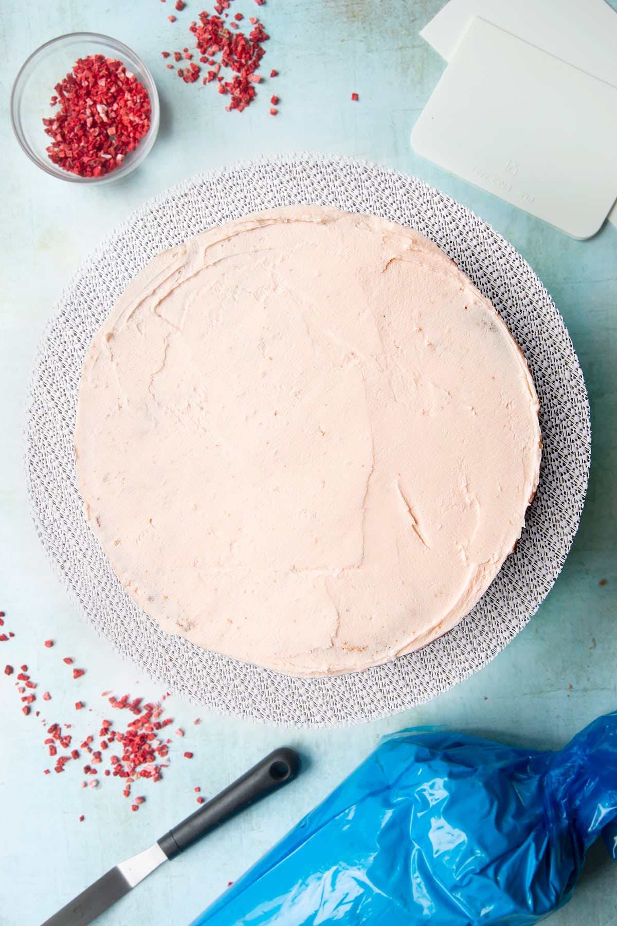 The three layers of a pink ombre cake from brightest to palest pink, stacked on a cake turntable. Pale pink frosting is sandwiched between the layers and coats the outside of the cake.
