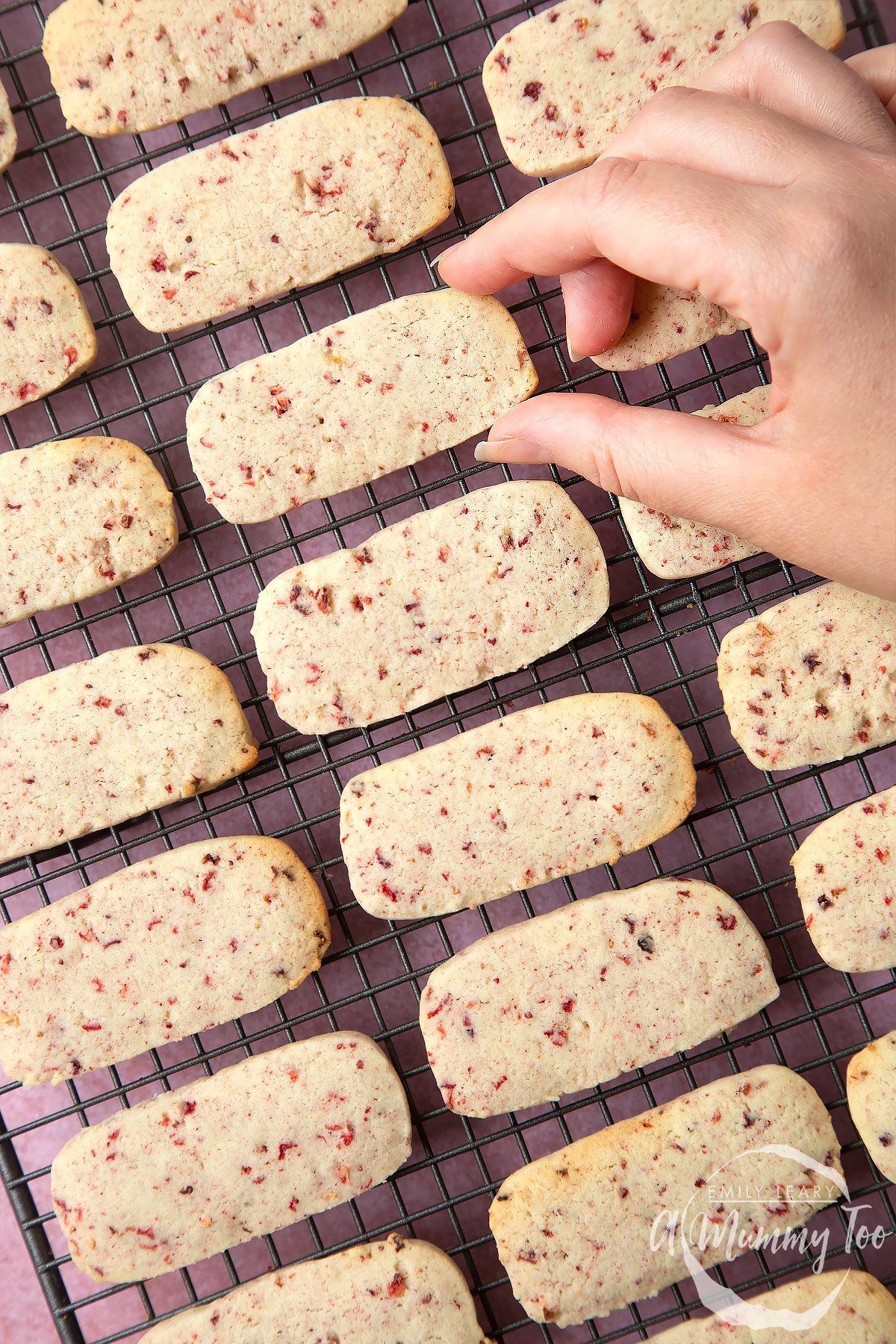 Strawberry biscuits on a cooling rack. Hand going in to pick one up.