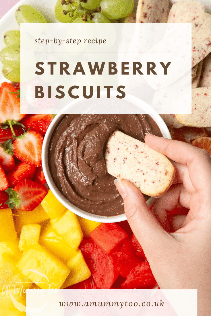 Strawberry biscuits being dipped into a chocolate sauce. Around the sides there's different fruits such as strawberries, melon and mango.