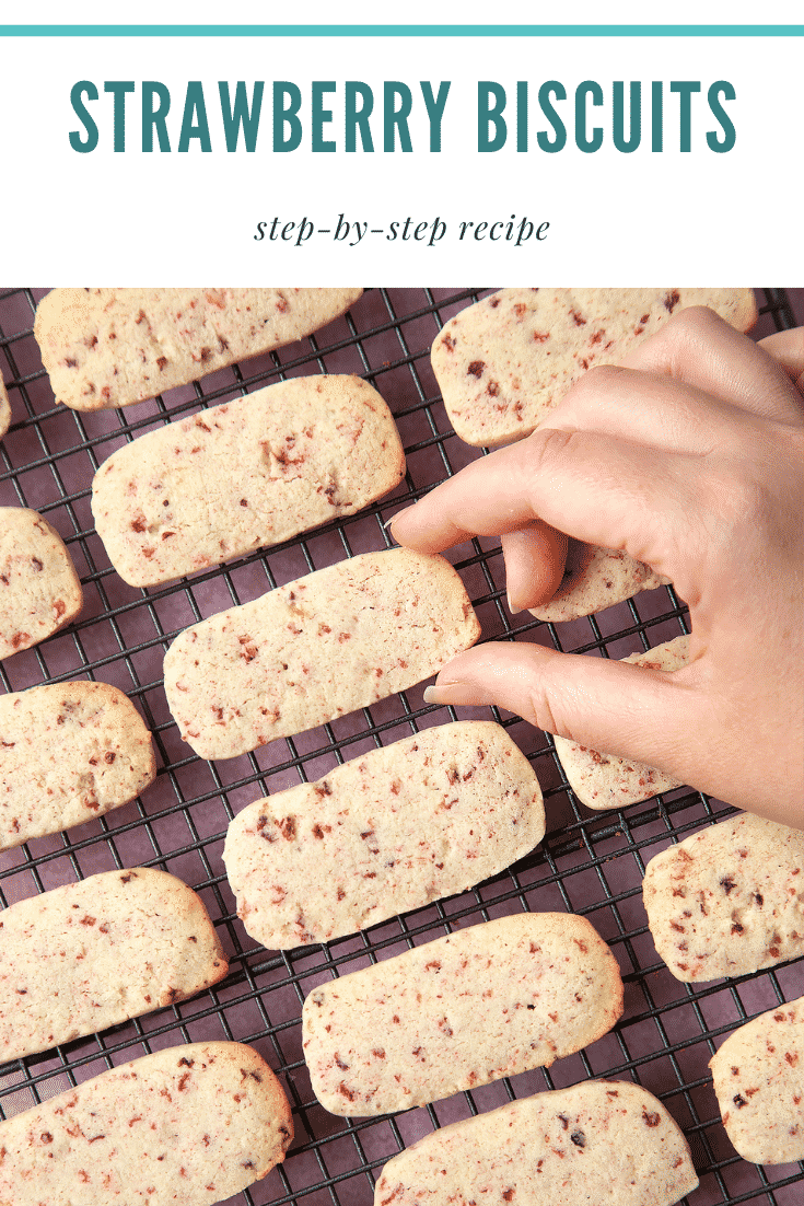 Strawberry biscuits on a wire rack cooling being picked up by a hand. At the top of the image there's some text. 