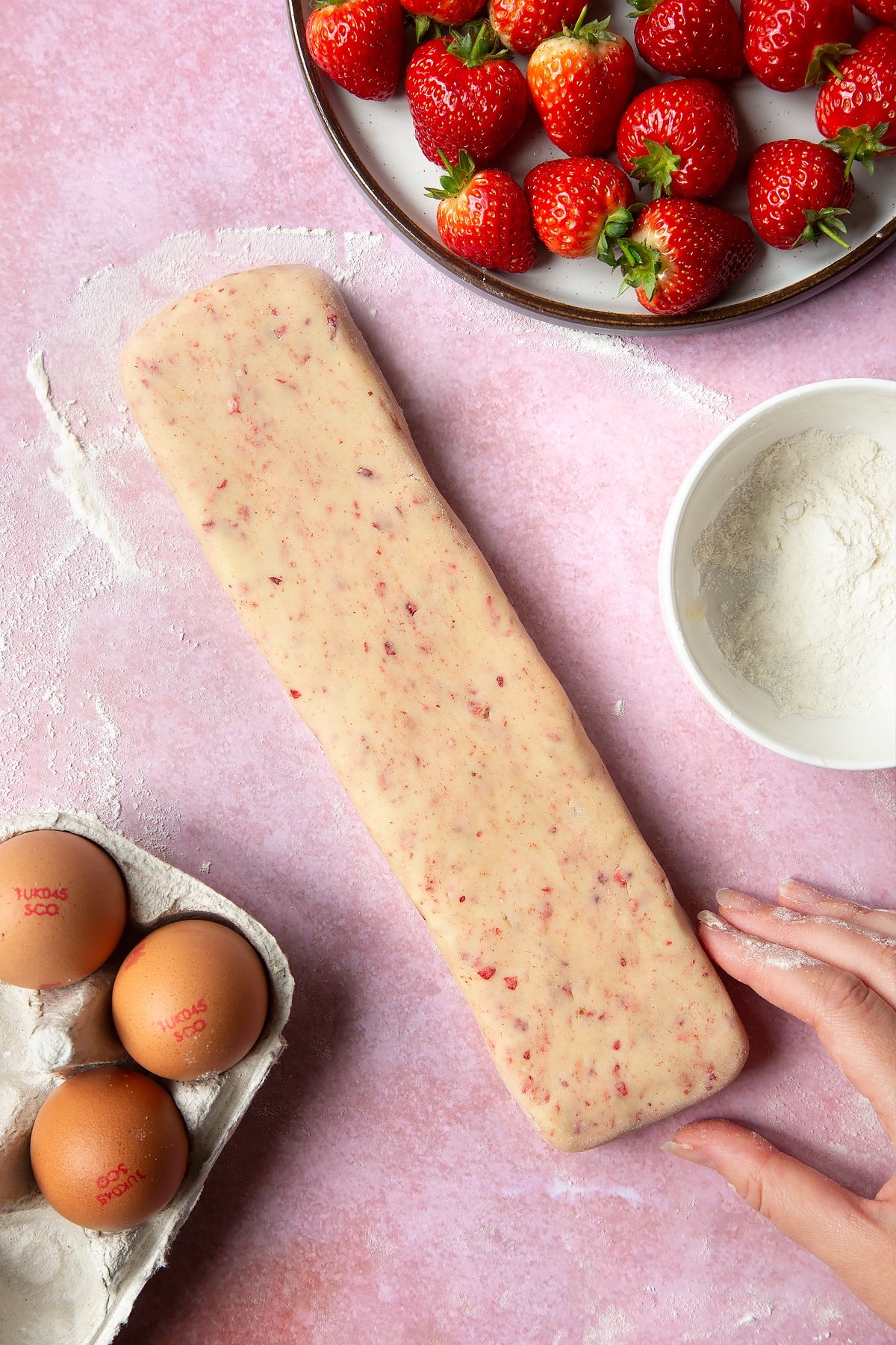 A floured surface with some strawberries on the side. The strawberry biscuit mixture has been rolled out into an oblong about 2cm tall, 2 inches wide and as long as the dough allows - mine came to around 30cm.