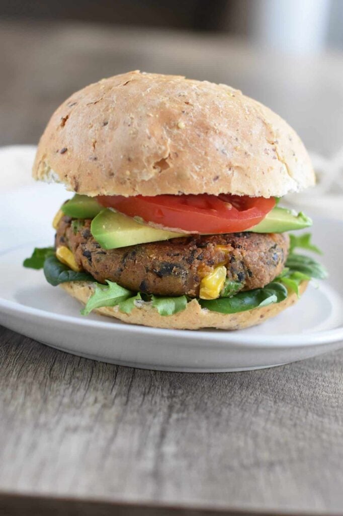 Sweet Potato Black Bean Burgers with avocado, tomato and lettuce sat on a plain white plate on a wooden table top.