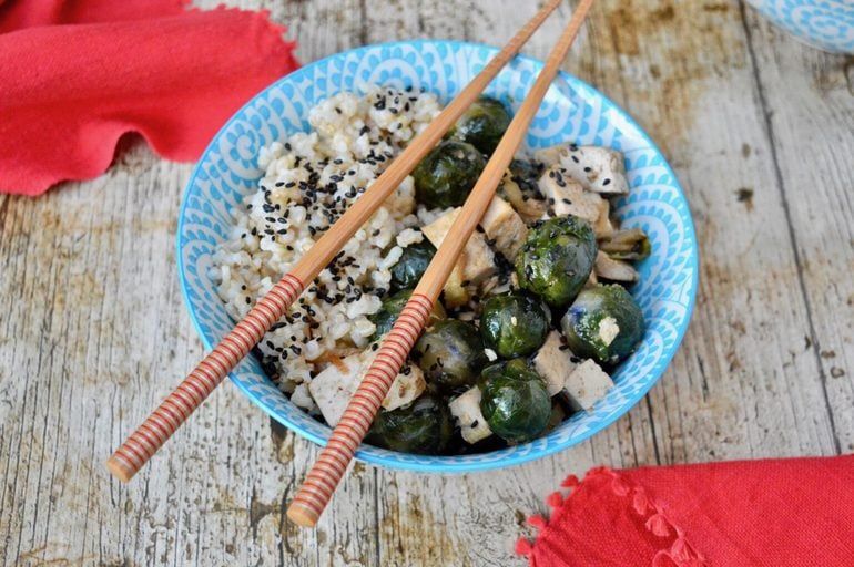 Teriyaki rice sits inside a blue decorative bowl on a wooden background. A pair of chopsticks lay across the top of the bowl.