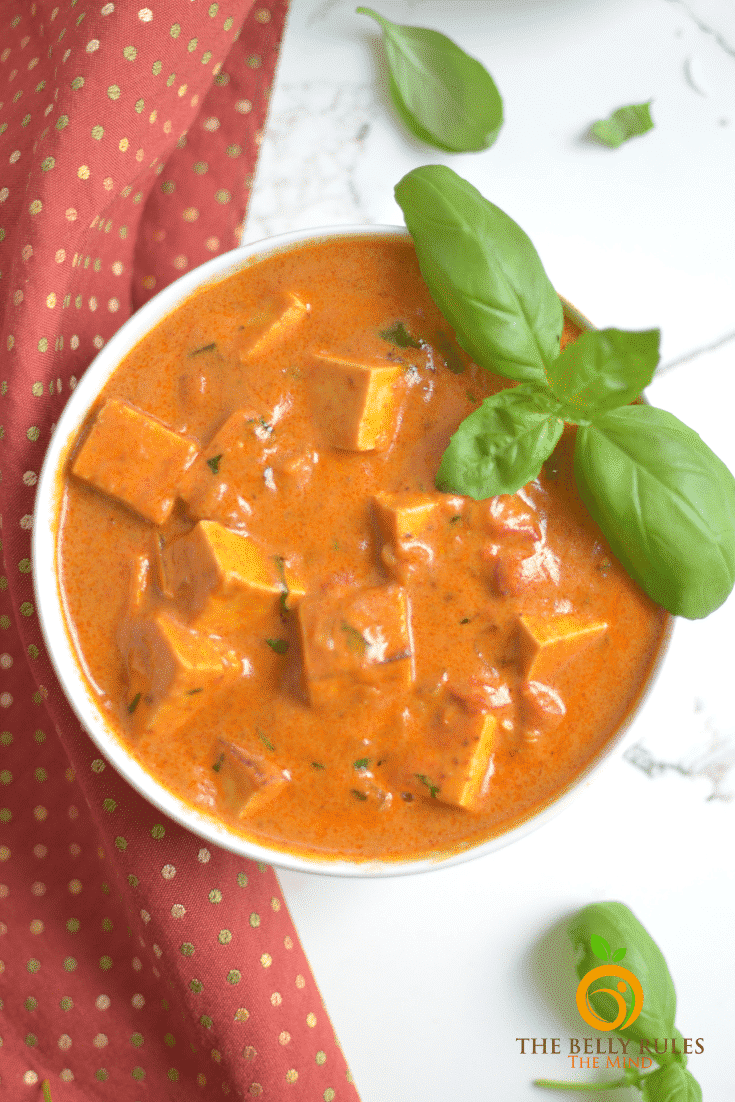 A bowl of vegan curry made from tofy pieces sits on top of a white background.