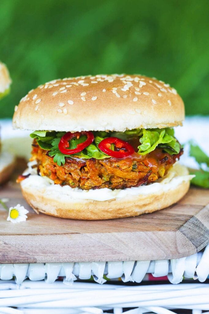 A Vegan Bhaji Burger sat on a wooden surface with chili peppers on show.