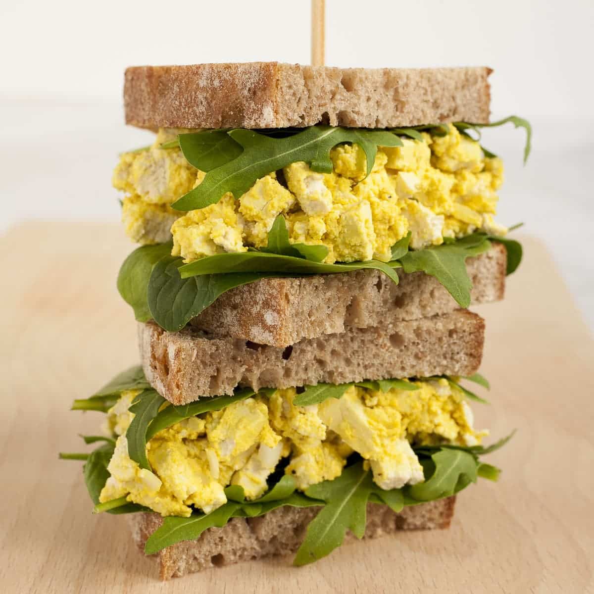 Vegan egg sandwiches stacked on top of one and other with a skewer through the top to keep them in place.