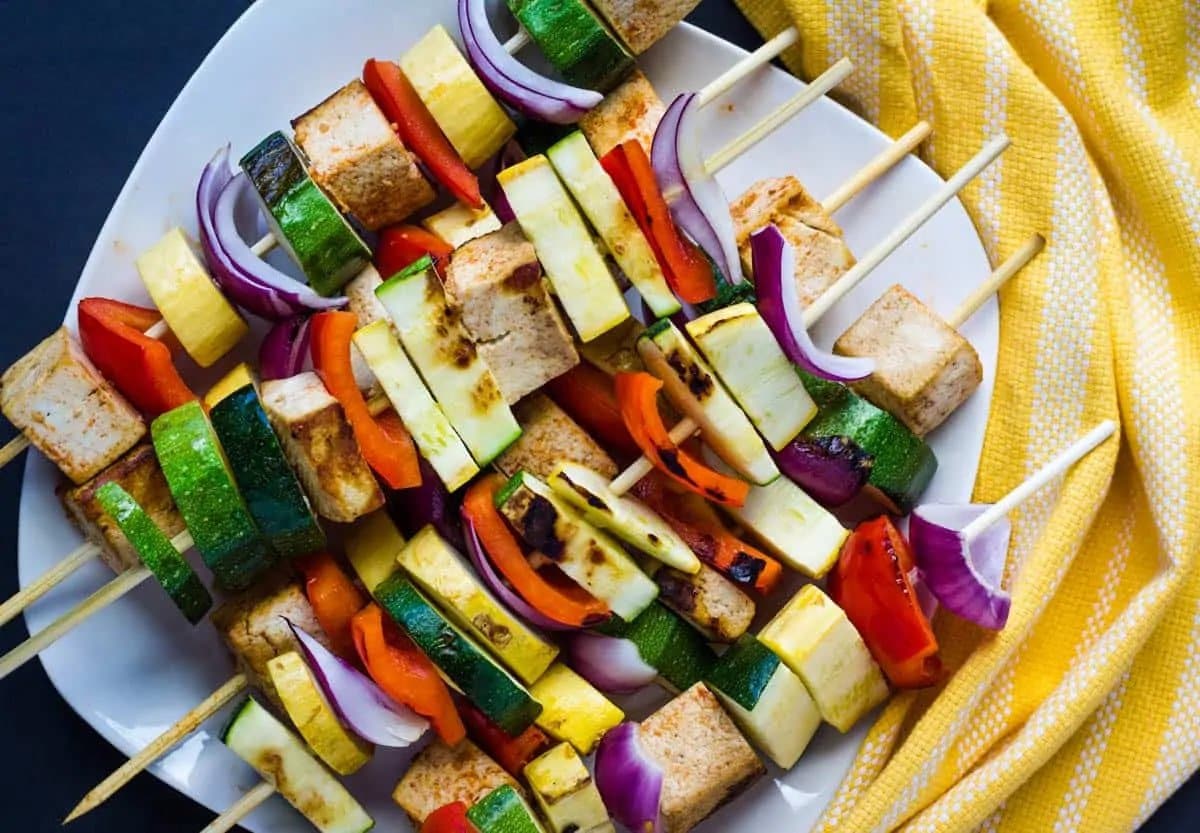 Kebab skewers made with tofy and vegetables stacked torgher on a white plate.