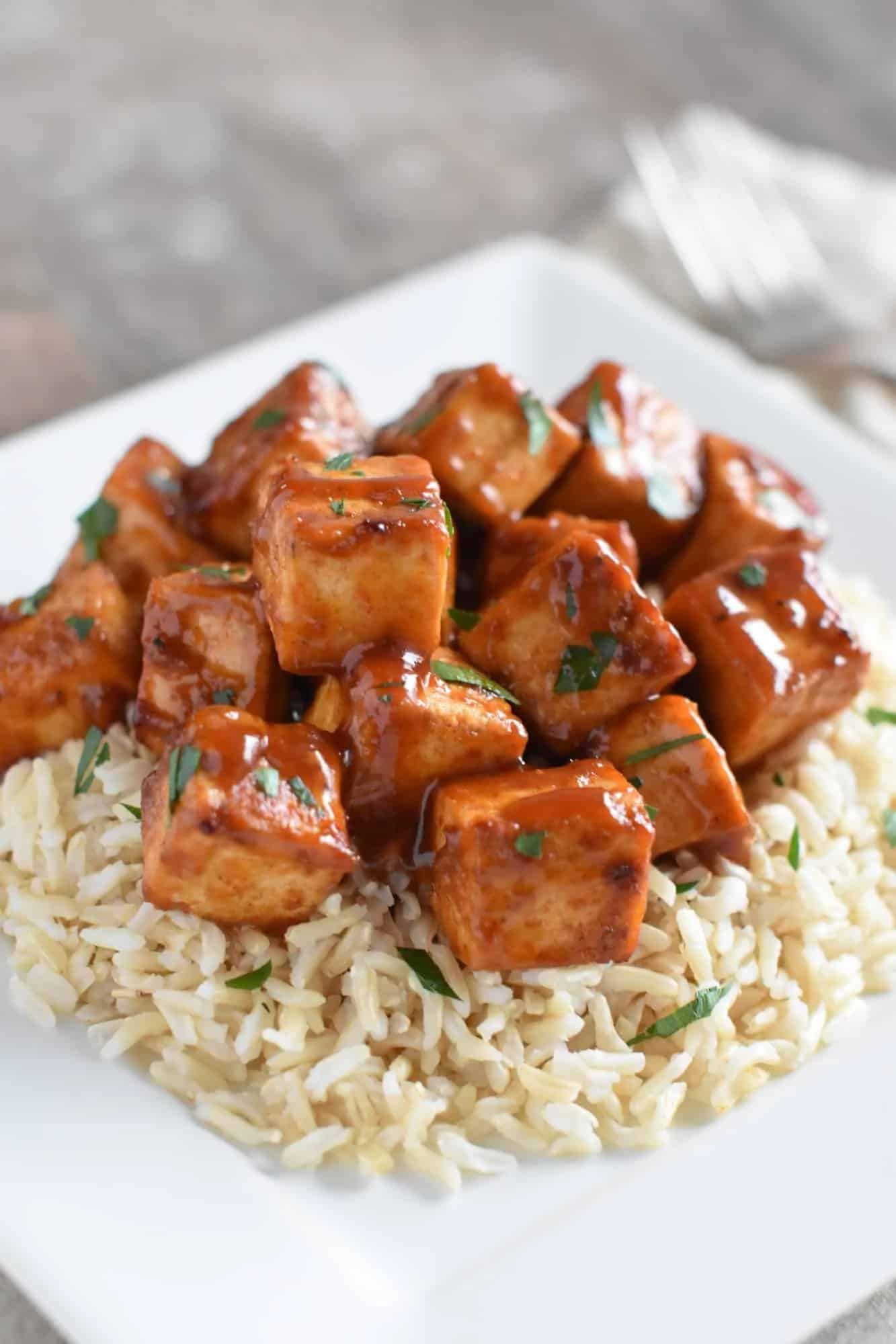 Baked tofu sits on a pile of white rice on a white plate.