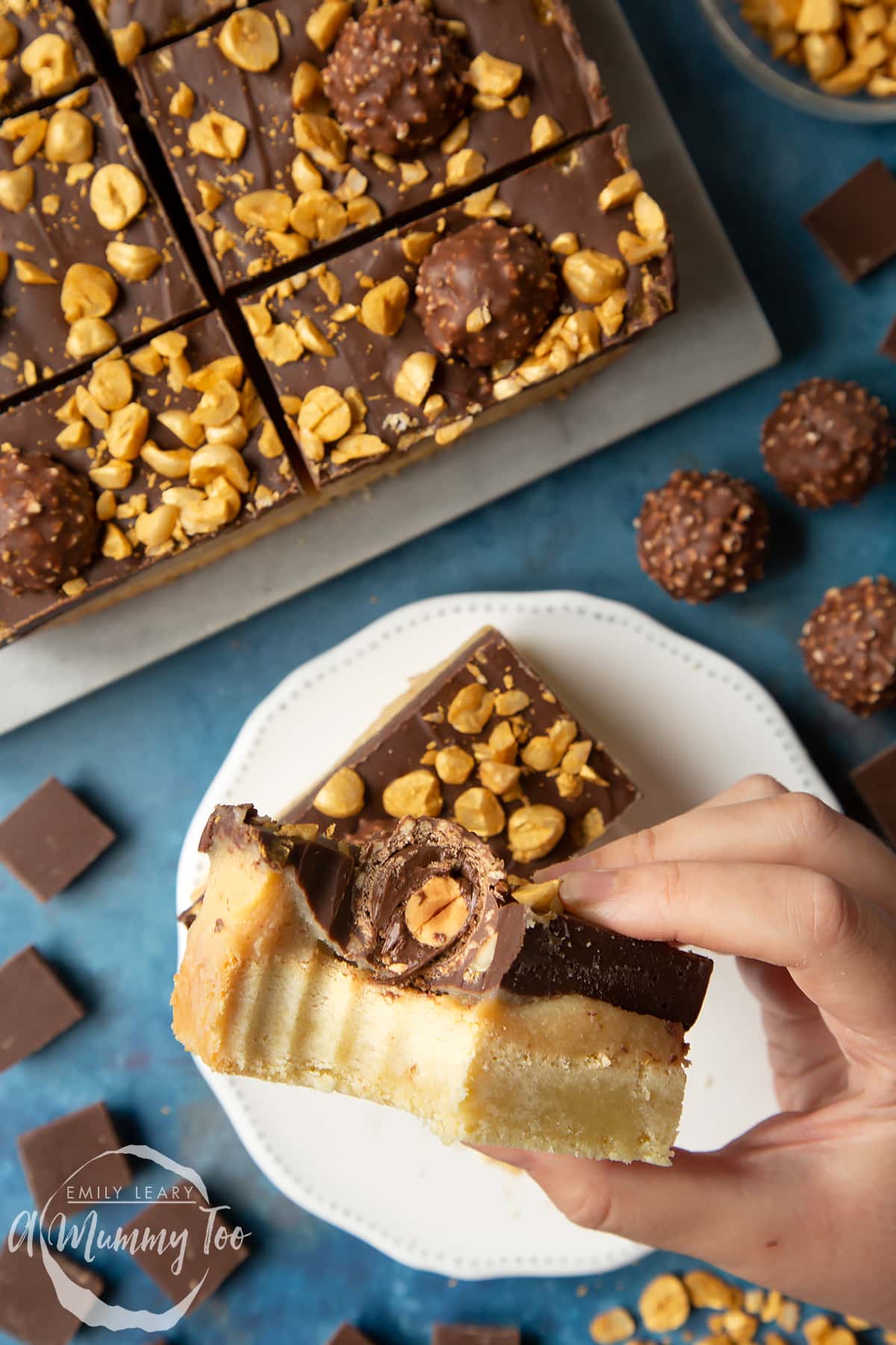 Hand holding a Ferrero Rocher slice with a bite out of it. Below is a plate and tray with more slices.