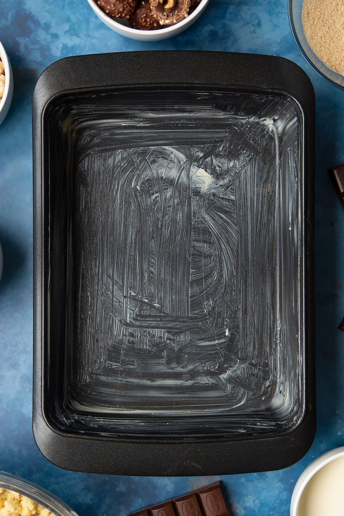 A greased tray. Ingredients to make a Ferrero Rocher slice surround the tray.