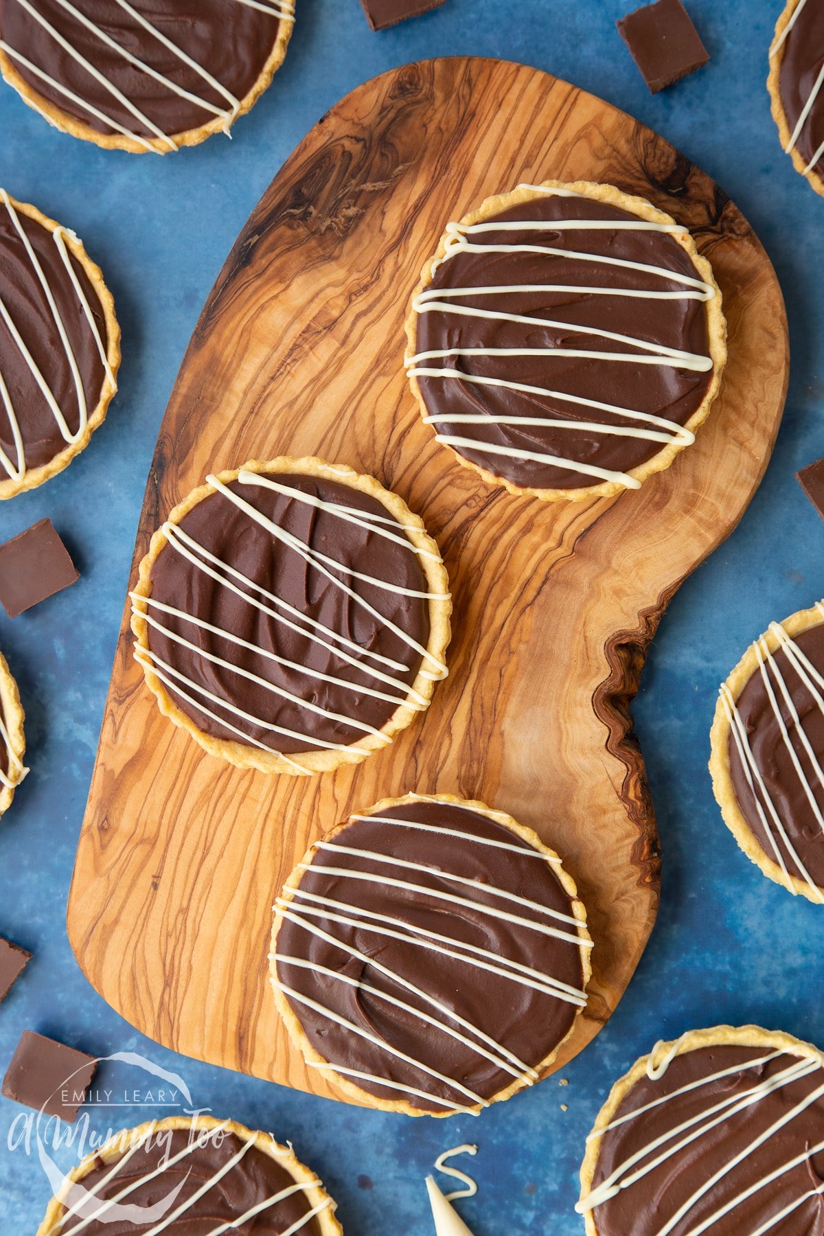 Three mini chocolate tarts on an olive board. 