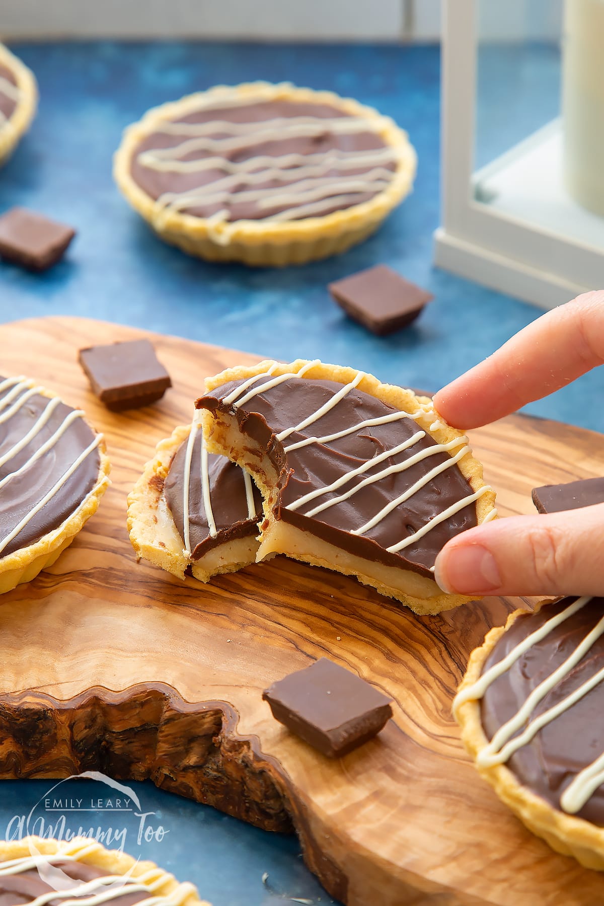 Mini chocolate tarts on a wooden board. One tart has been cut in half. A hand holds a half, which has a bite out of it.