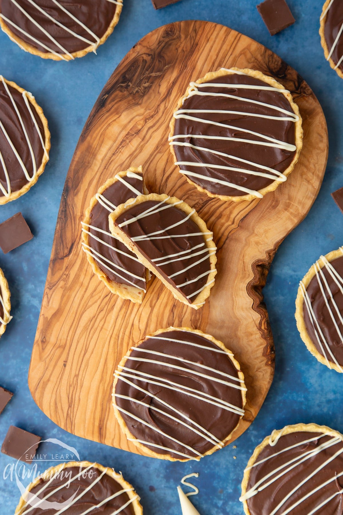 Mini chocolate tarts on an olive board. One tart has been cut in half.