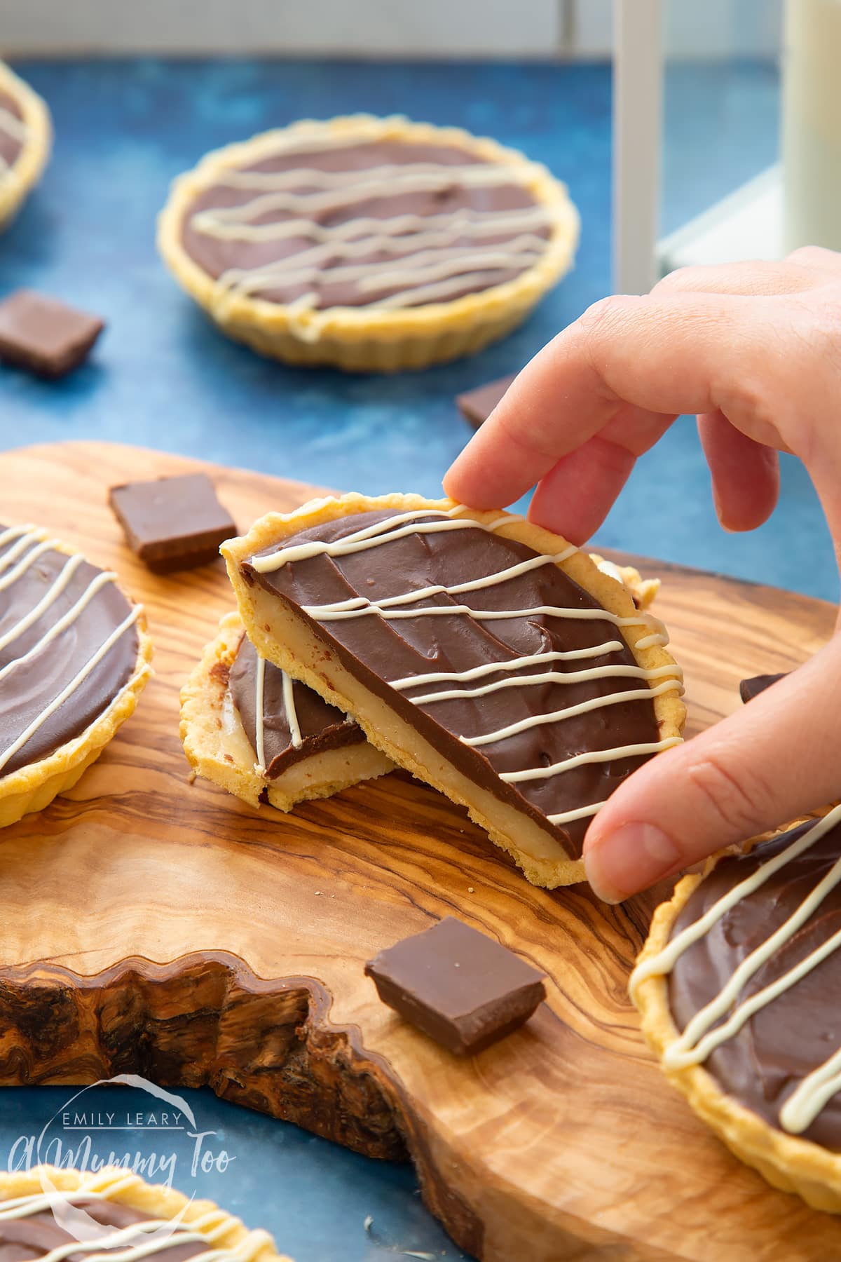 Mini chocolate tarts on an olive board. One tart has been cut in half. A hand holds a piece.