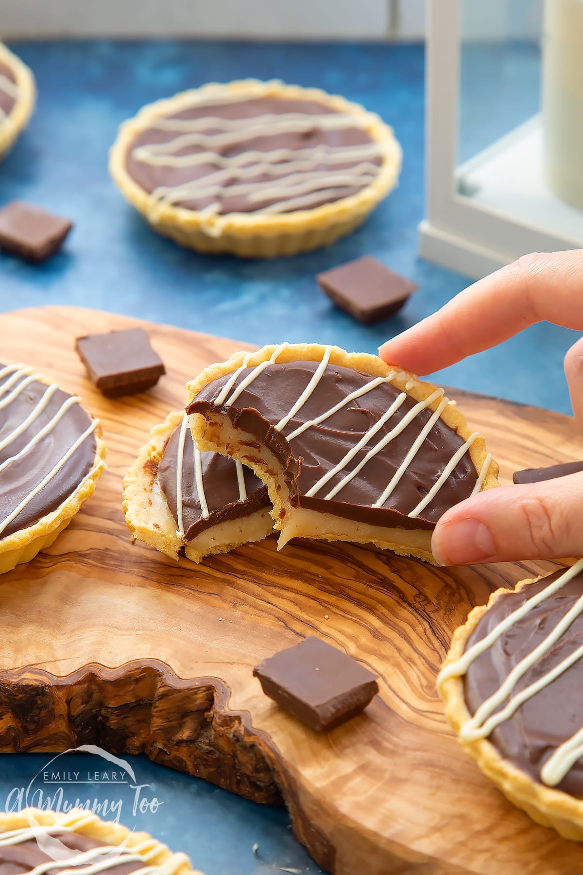 Mini chocolate tarts on an olive board. One tart has been cut in half. A hand holds a half, which has a bite out of it.