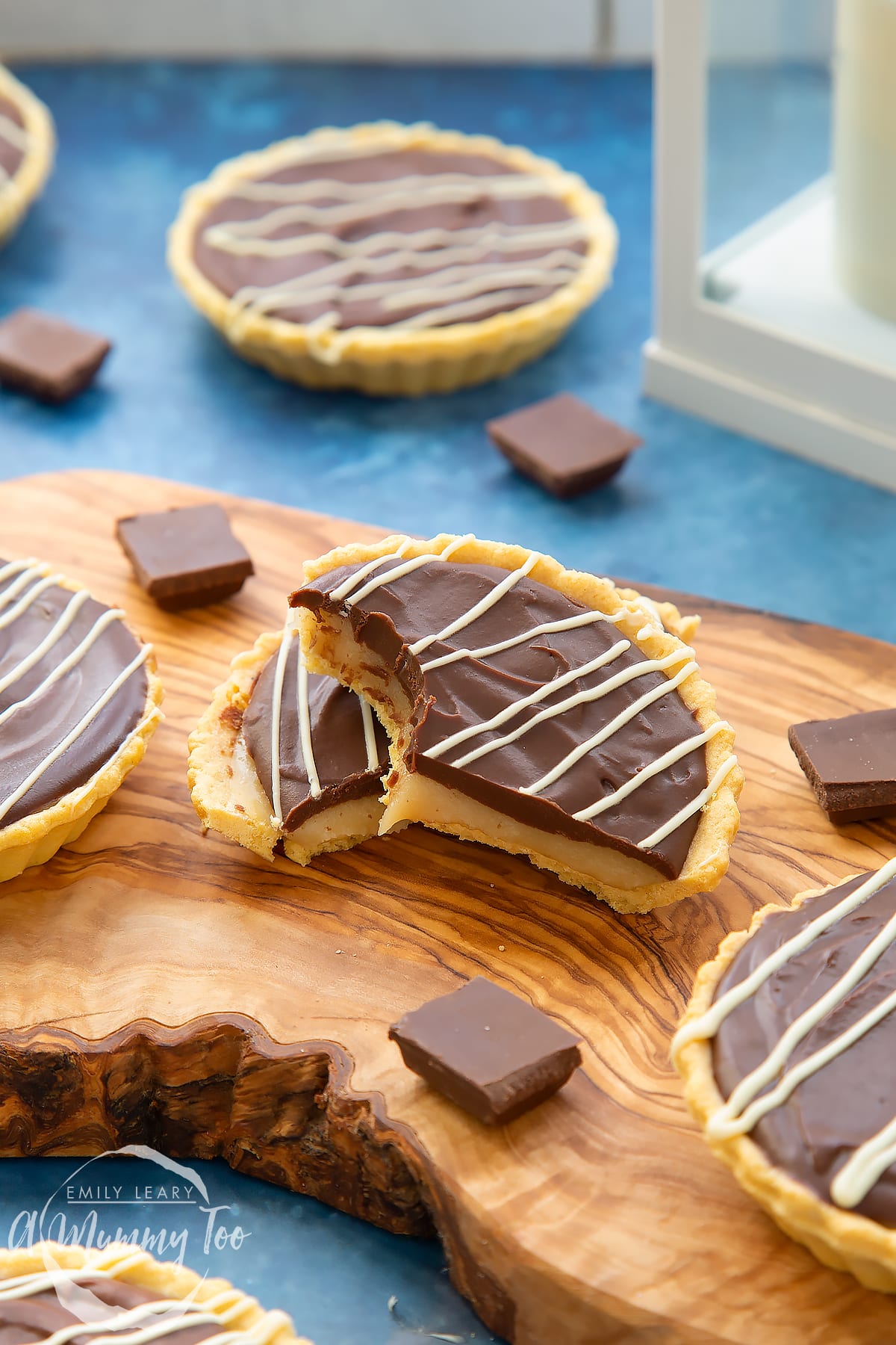 Mini chocolate tarts on an olive board. One tart has been cut in half. Once half has a bite out of it.