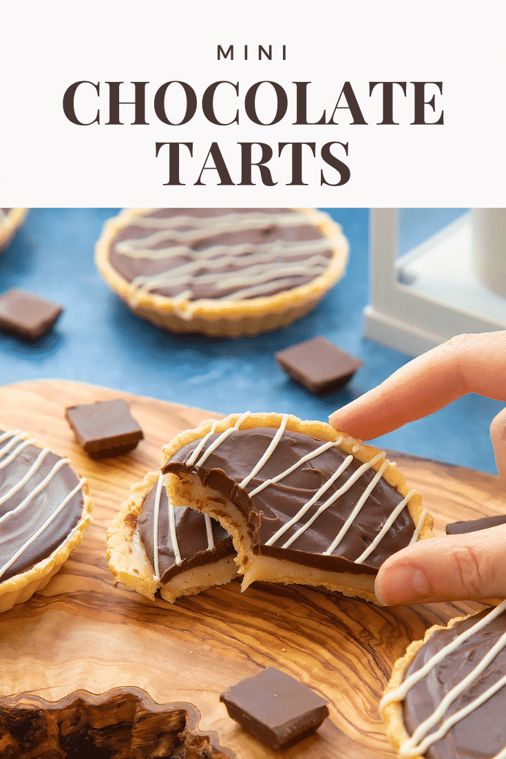 Mini chocolate tarts on an olive board. One tart has been cut in half. A hand holds a half, which has a bite out of it. Caption reads: mini chocolate tarts