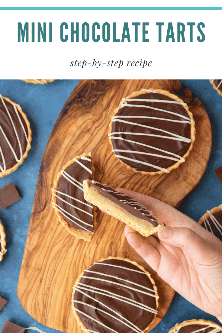 Mini chocolate tarts on an olive board. One tart has been cut in half. A hand holds a half. Caption reads: mini chocolate tarts step-by-step recipe