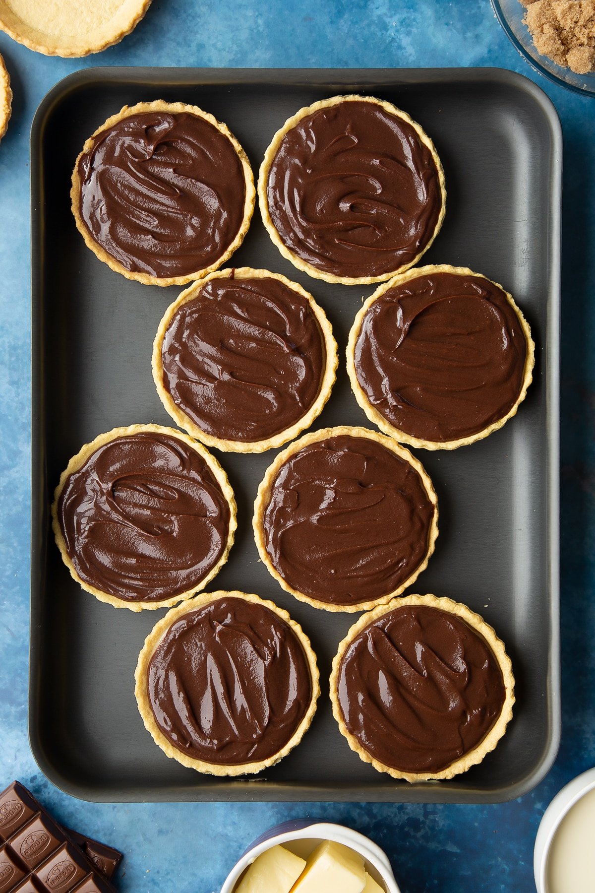 Mini chocolate tarts filed with caramel and chocolate ganache on a large metal tray. 