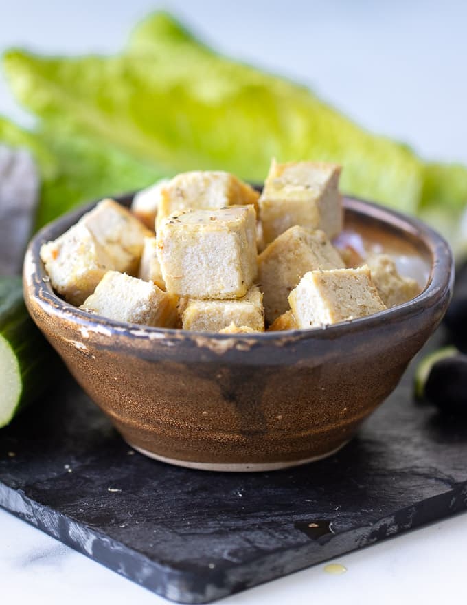 Vegan feta cheese made from tofu stacked in a bowl with a lettace leaf in the background. 