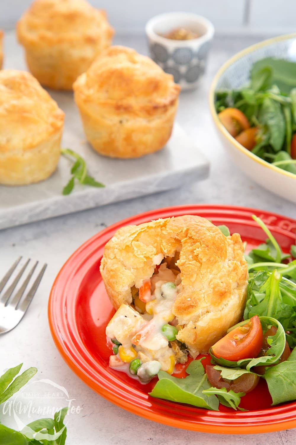 Cut open tofu and vegetable mini pie on a red plate. Three additional pies are in the background.