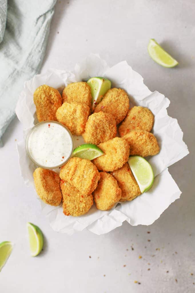 Tofu baked nuggets covered in bed crumbs served on a white table with a side of lemon and a side of dipping sauce. 