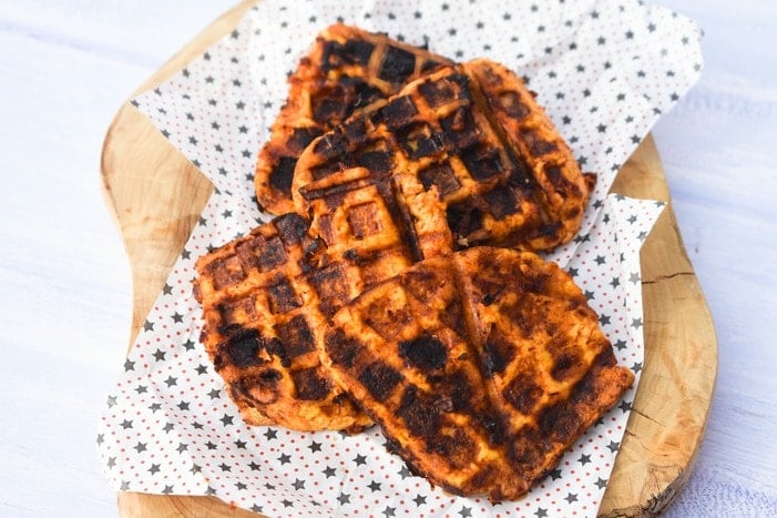 Three waffles sit on sheets of baking paper ontop of a chopping board.