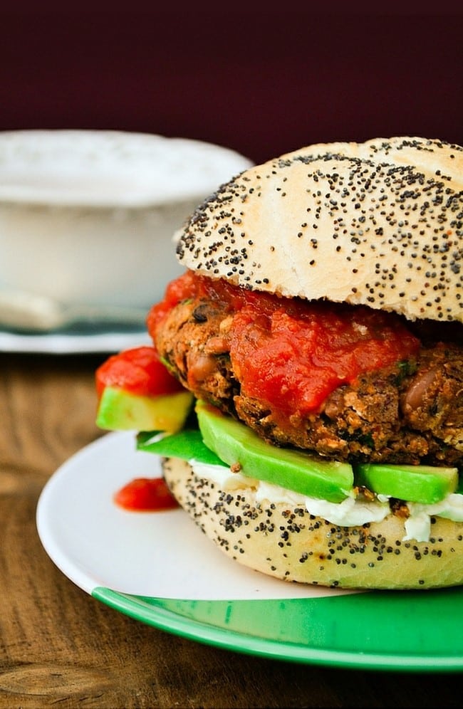 Spicy vegan burger inside a sesame seed coated bun on a white and green plate.