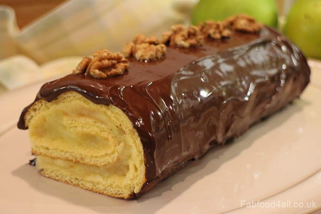 Apple and chocolate spelt Swiss roll on a white plate with a decorative napkin / tea towel in the background.