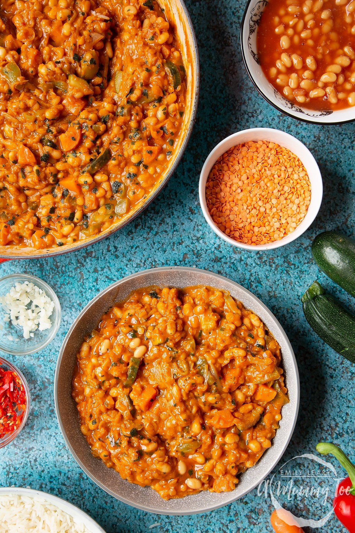 Baked bean curry served in a grey bowl. More curry is shown in a pan to the side.