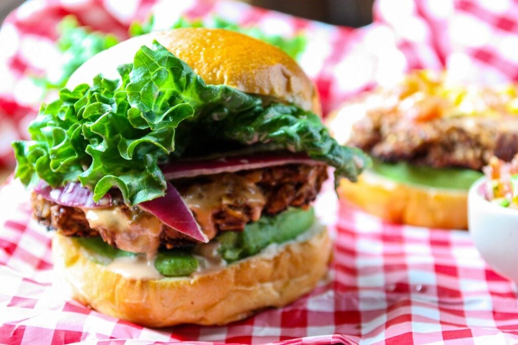 Bean and lentil veggie burger topped with onion and lettuce on a red and white checked napkin