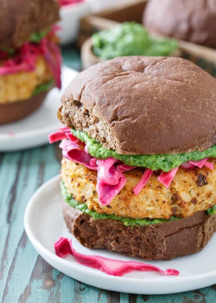 A cheddar cauliflower burger in the foreground on a white plate with two additional cheddar cauliflower burgers in the background.