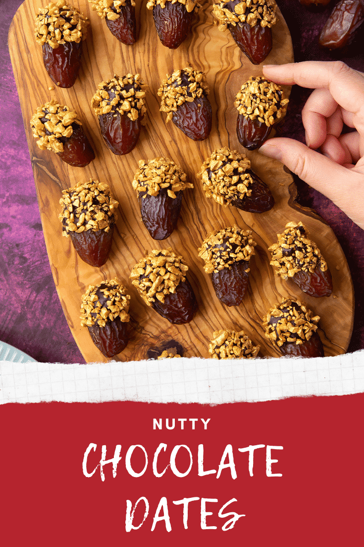 Medjool dates on a wooden board and. They have been dipped in chocolate and studded with gold chopped nuts. A hand reaches for one. Caption reads: nutty chocolate dates