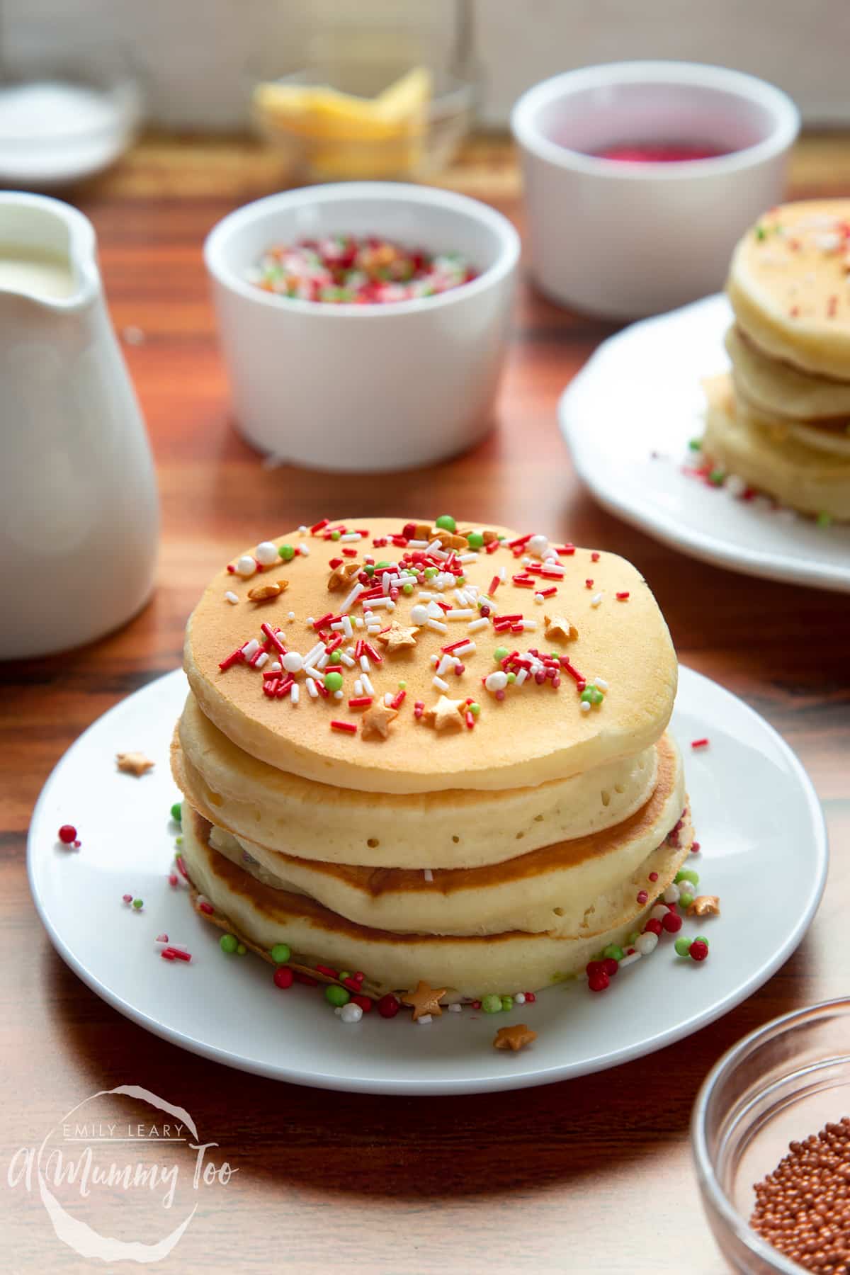 A tall stack of Christmas morning pancakes, stacked on a white plate, scattered with festive sprinkles.