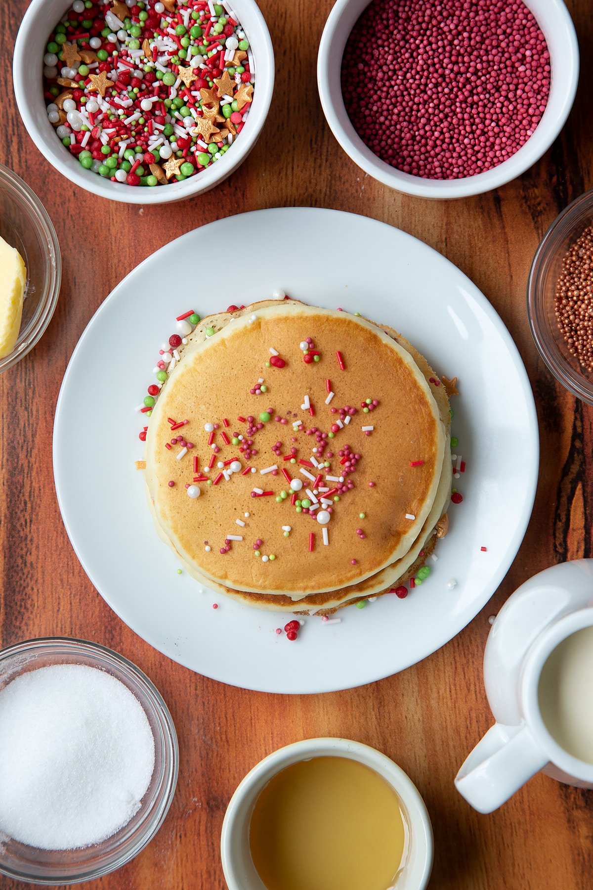 Two Christmas morning pancakes, stacked on a white plate, scattered with festive sprinkles.