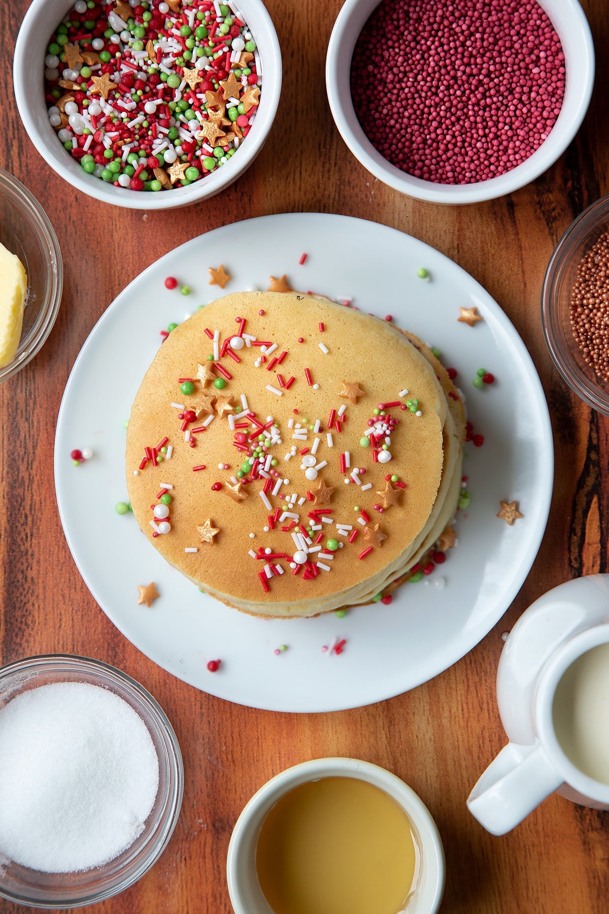 A stack of Christmas morning pancakes, stacked on a white plate, scattered with festive sprinkles.