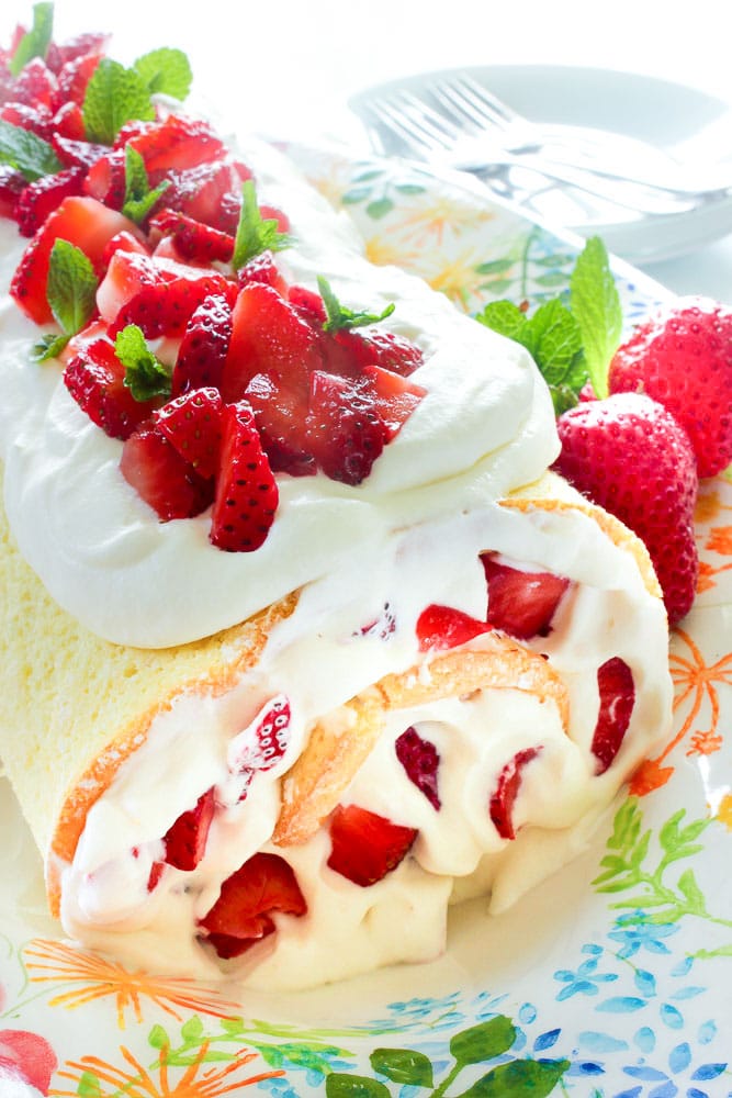 Strawberry Swiss roll decorated with chopped strawberries on a decorative white plate.