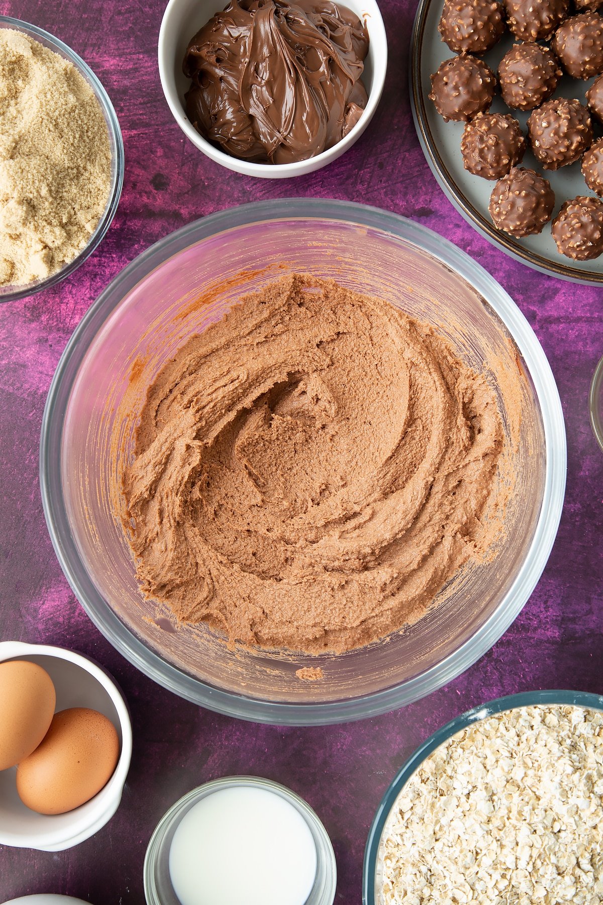 Soft brown sugar, Nutella and butter beaten together in a large mixing bowl. Ingredients to make Ferrero Rocher cookies surround the bowl.