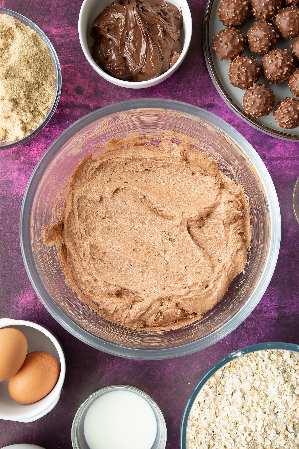 Soft brown sugar, Nutella, butter, eggs and milk beaten together in a large mixing bowl. Ingredients to make Ferrero Rocher cookies surround the bowl.