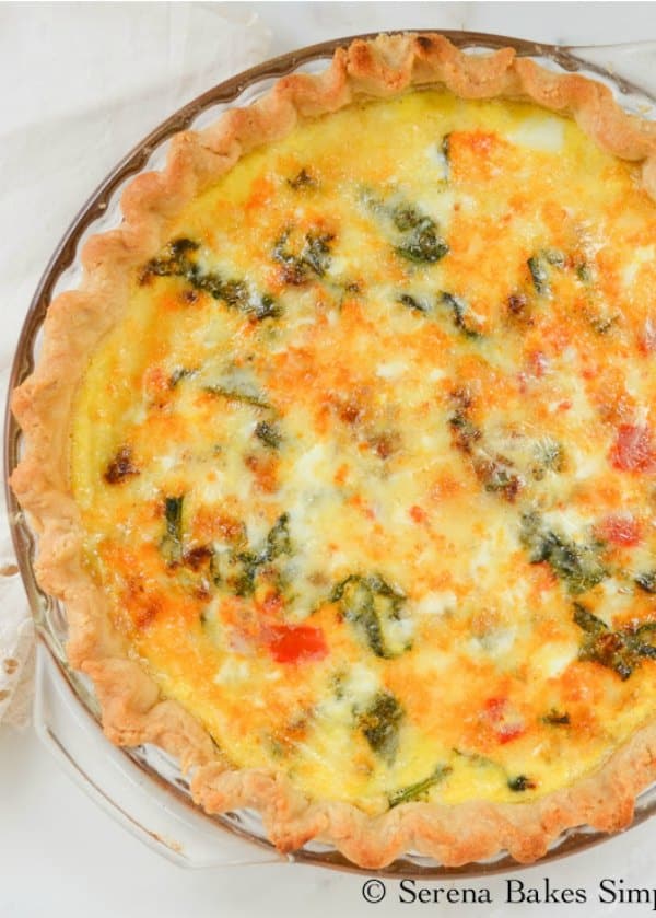 A Fontina Chorizo Spinach Quiche inside a clear pyrex dish on a white background. This is a close up photo which cuts off the top right hand corner of the quiche. 