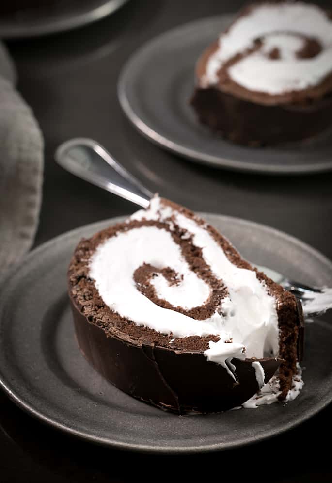 Gluten free Swiss roll slice on a dark grey plate with a fork on the side of the plate. The plte sits on a dark black surface.