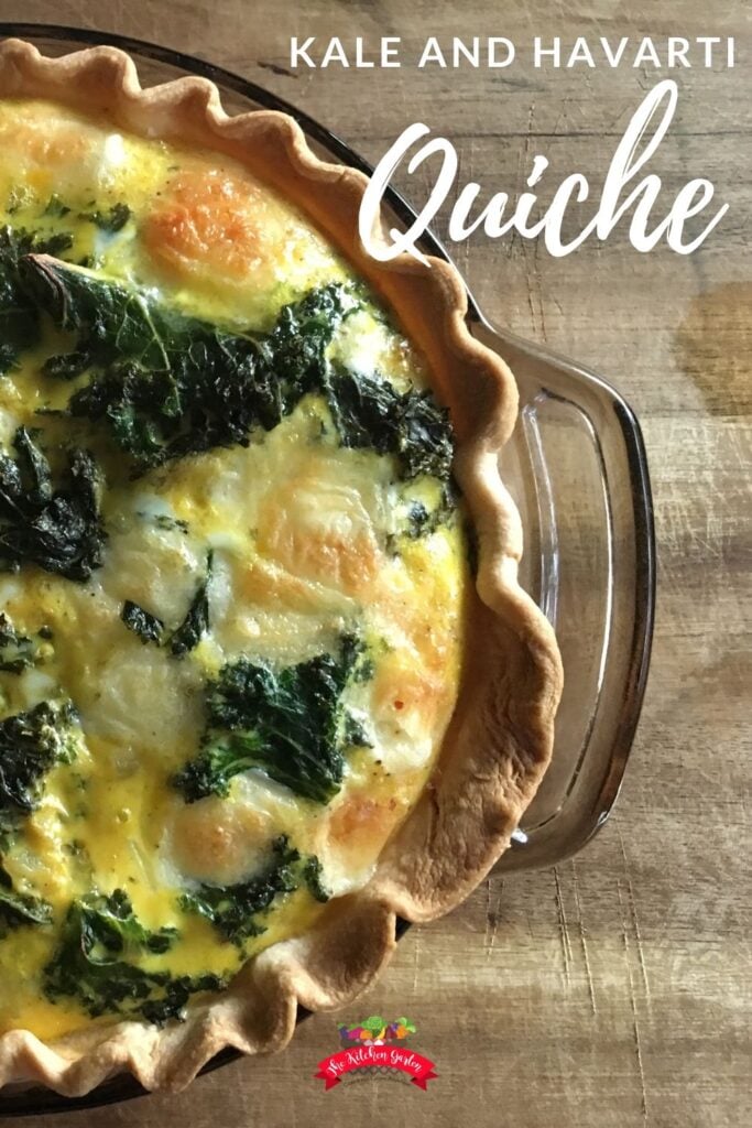 A whole kale and havarti quiche sites inside a ceramic dish on top of a wooden chopping board. The quiche is situated to the left of the image and cuts off the edes. 