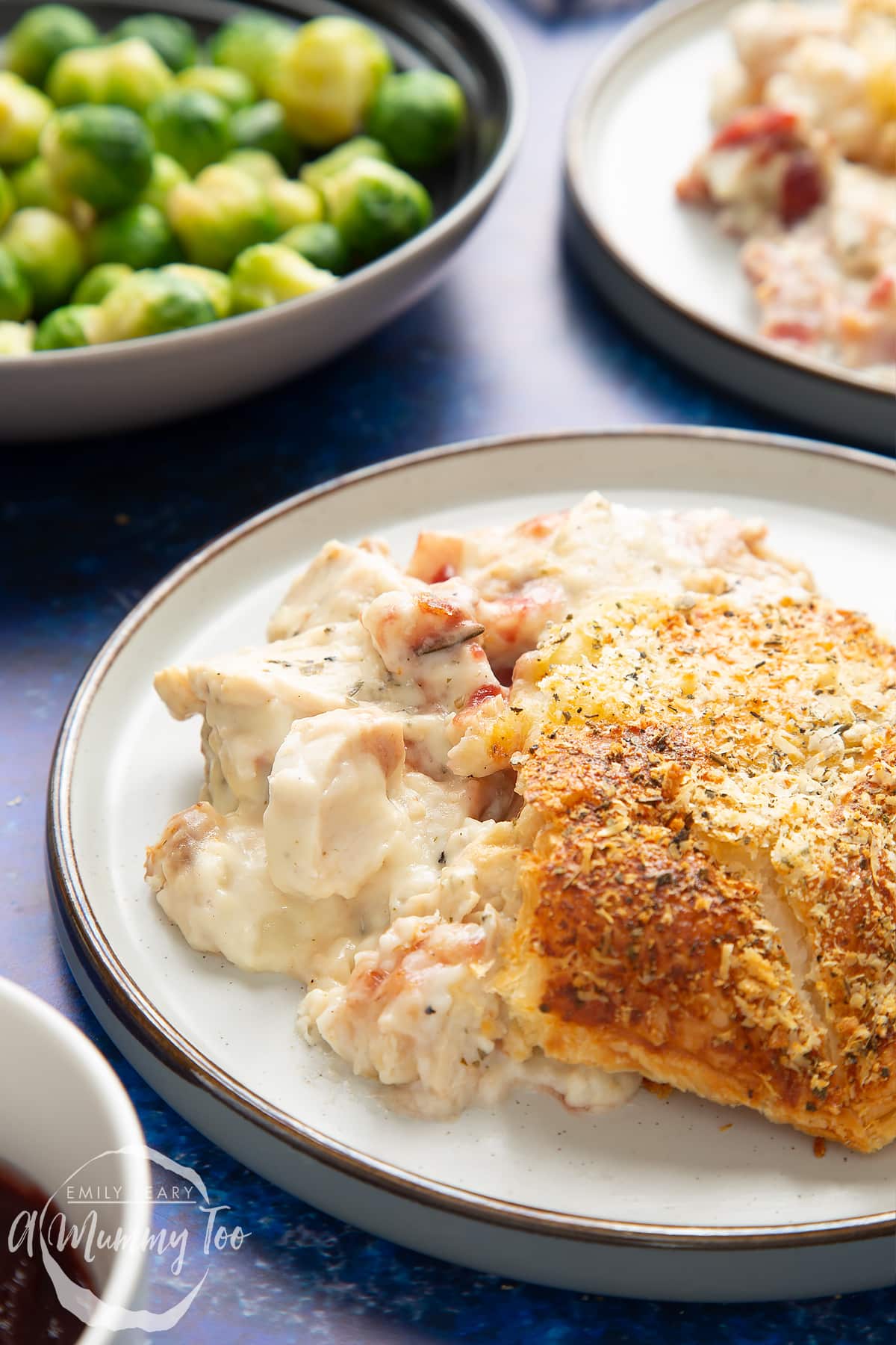 A generous portion of cooked leftover Christmas dinner pie served to a plate with a golden puff pastry top. A bowl of sprouts is in the background.