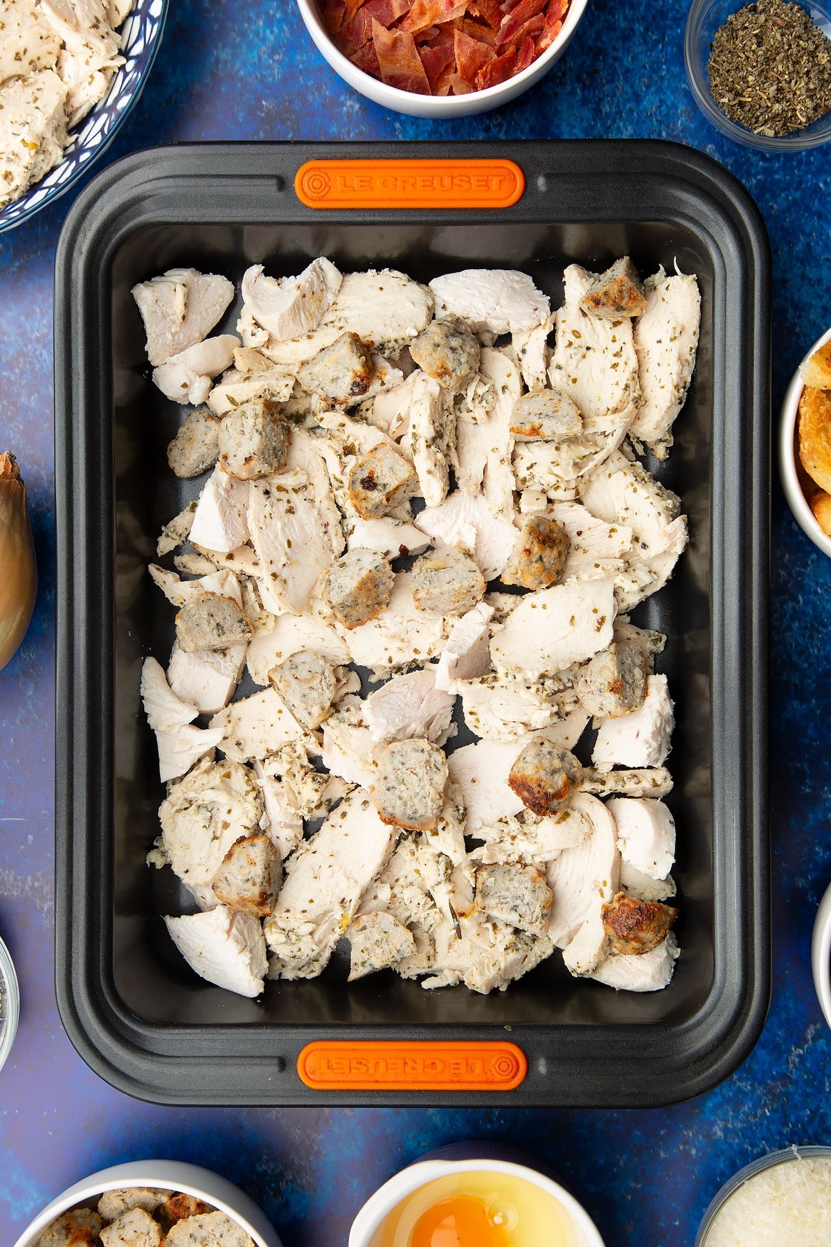 Chopped cooked turkey and stuffing in a roasting dish. Ingredients to make a leftover Christmas dinner pie surround the tray.